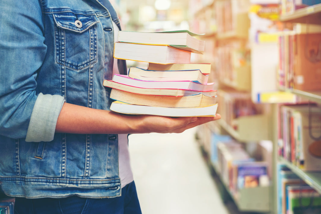 student carrying stack of books in store