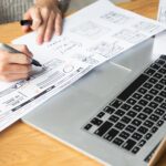 person taking notes next to laptop