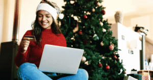 Woman smiling shopping online in front of Christmas tree